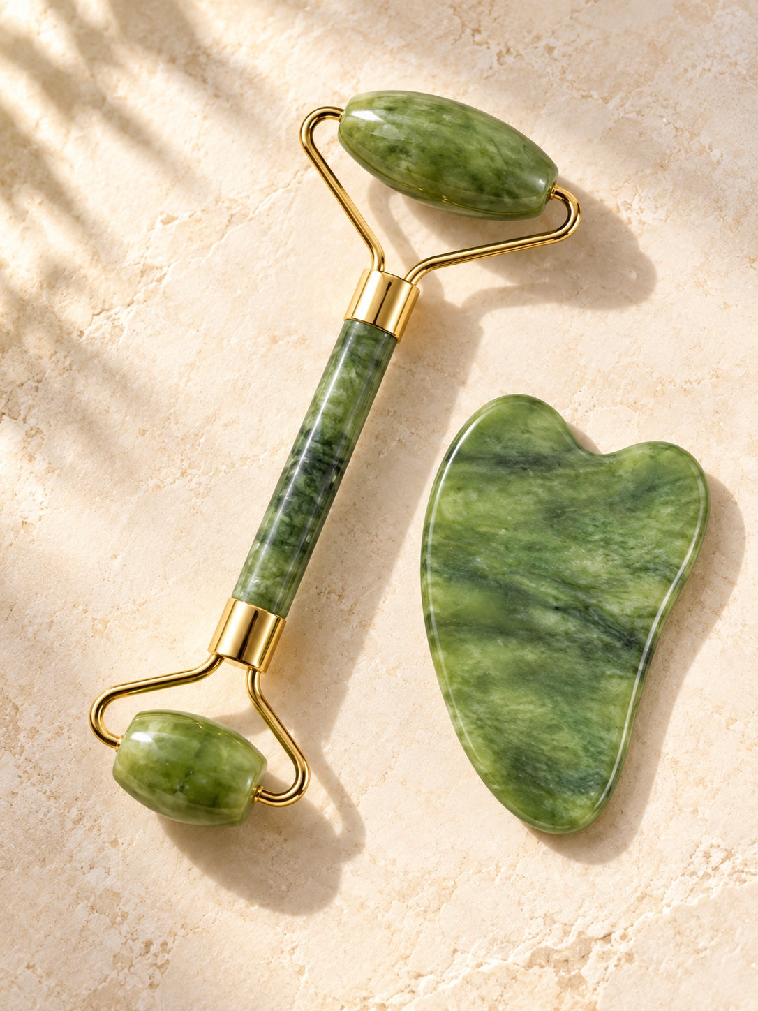 Jade double-ended roller and heart gua sha on cream stone in soft sunlight