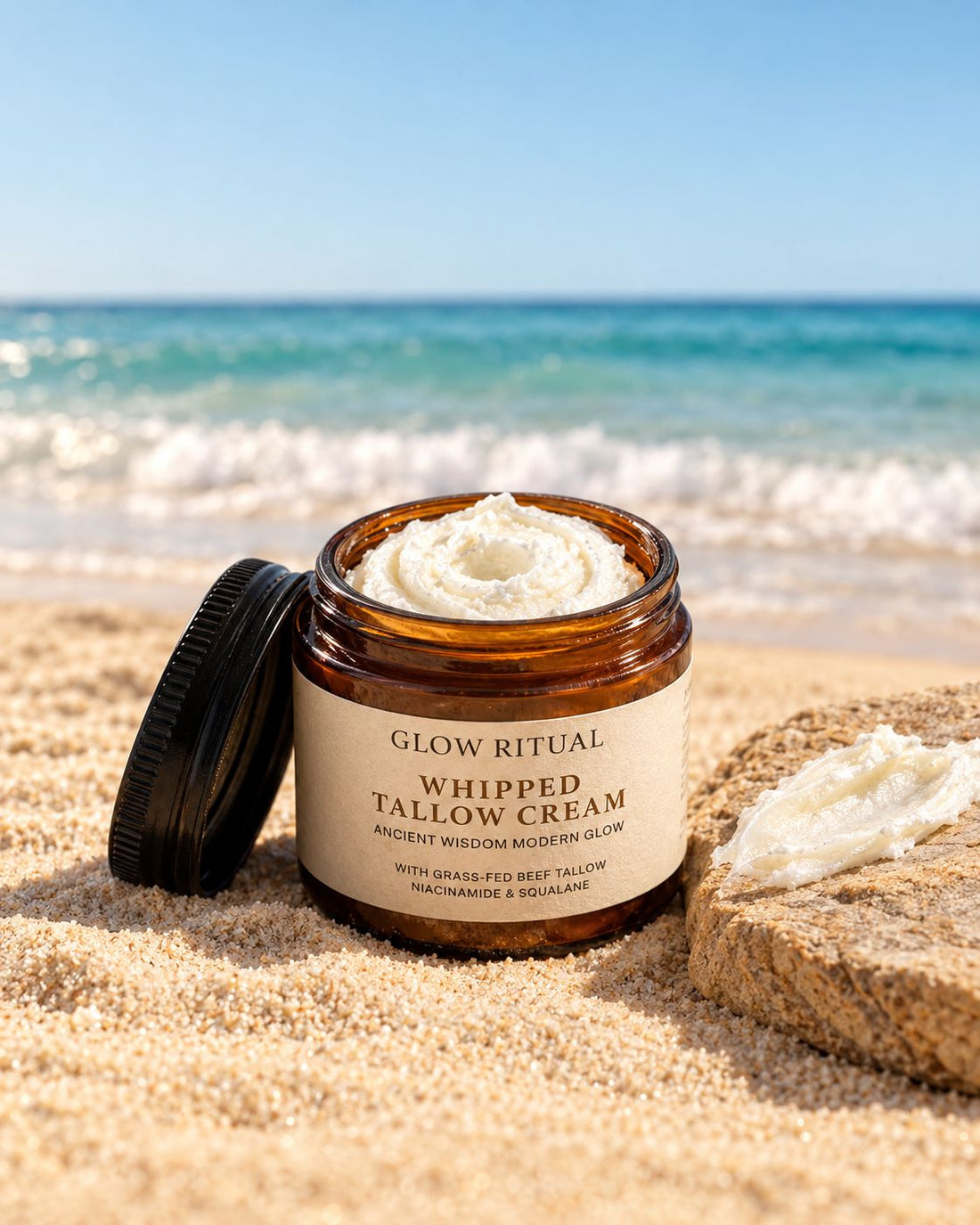 Open jar of Glow Ritual Whipped Tallow Cream on the sand