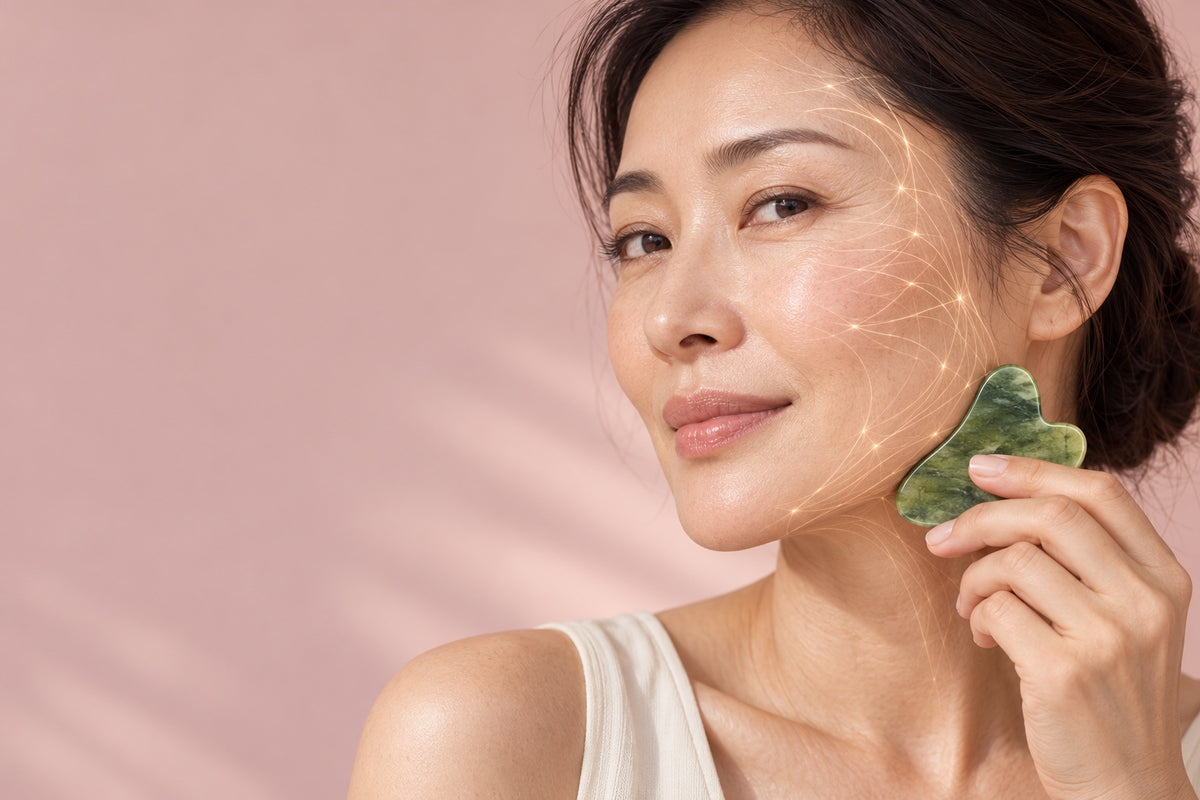 Woman gliding the jade gua sha along her jawline on a blush background