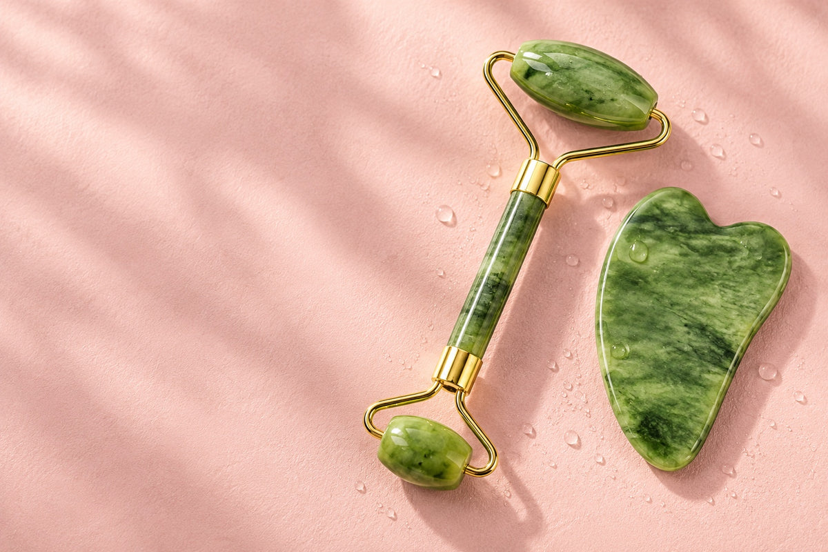 Jade roller and gua sha on blush pink with water droplets