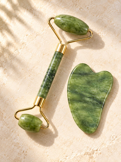 Jade double-ended roller and heart gua sha on cream stone in soft sunlight